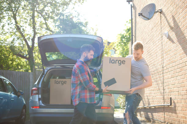 Deux jeunes hommes qui chargent des cartons de déménagement dans le coffre d'une voiture